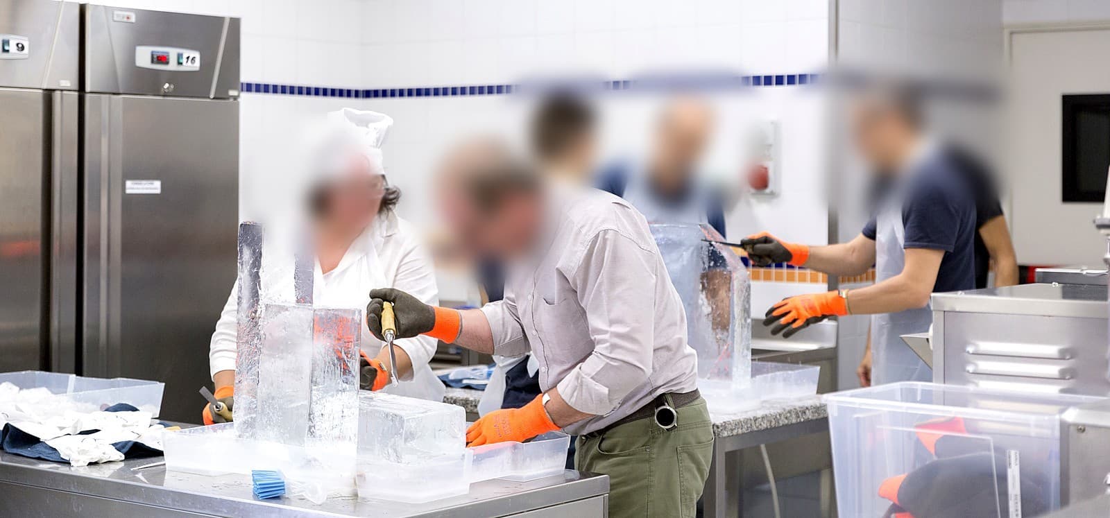 Partecipanti con guanti da lavoro che scolpiscono blocchi di ghiaccio con scalpelli